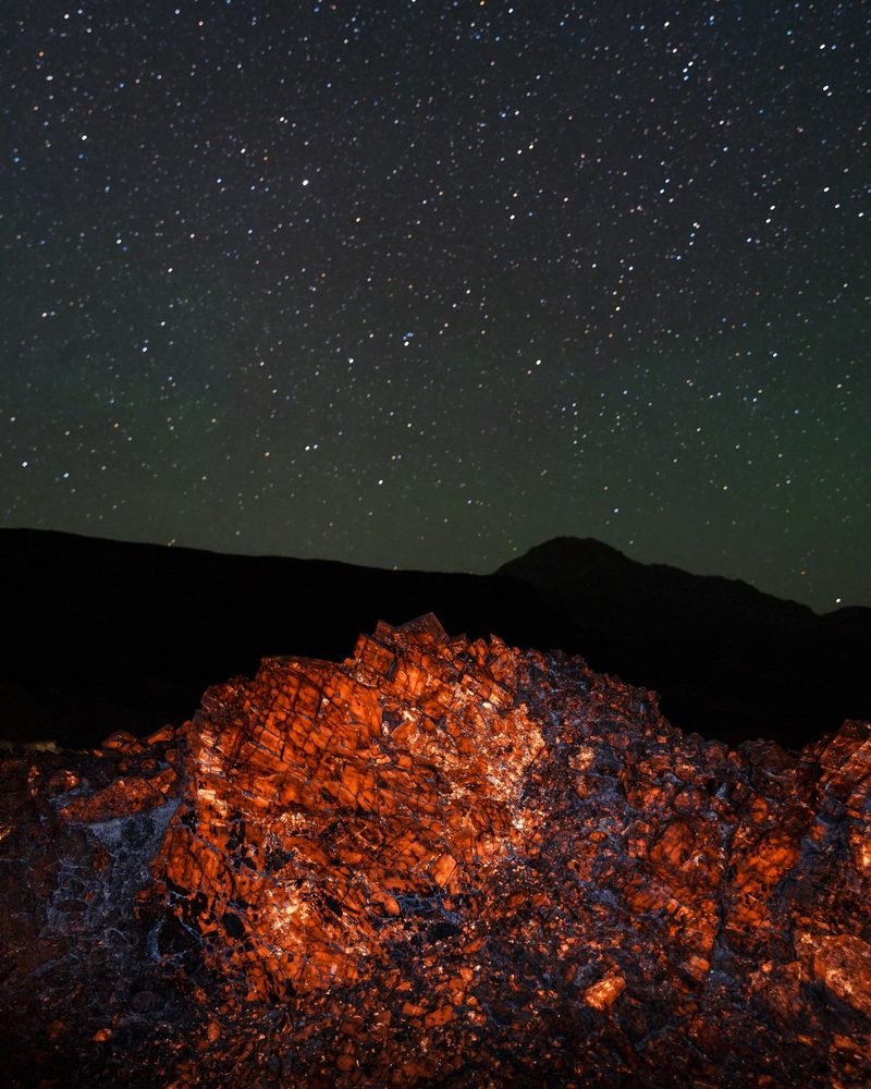 A mound of rocks glowing bright orange on the open desert floor under a starry sky.